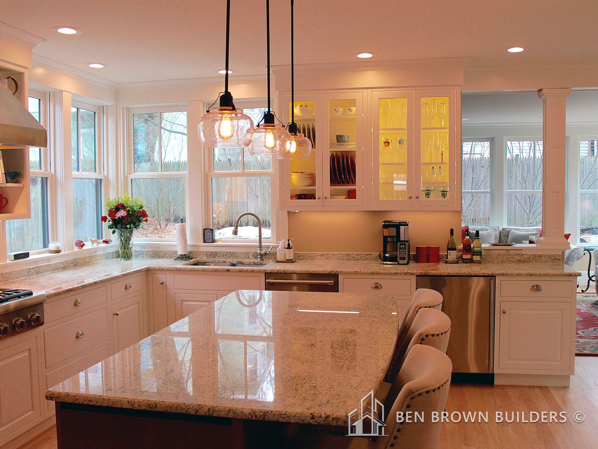 Bright kitchen interior with granite island, pendant lights, and a view to a cozy living area