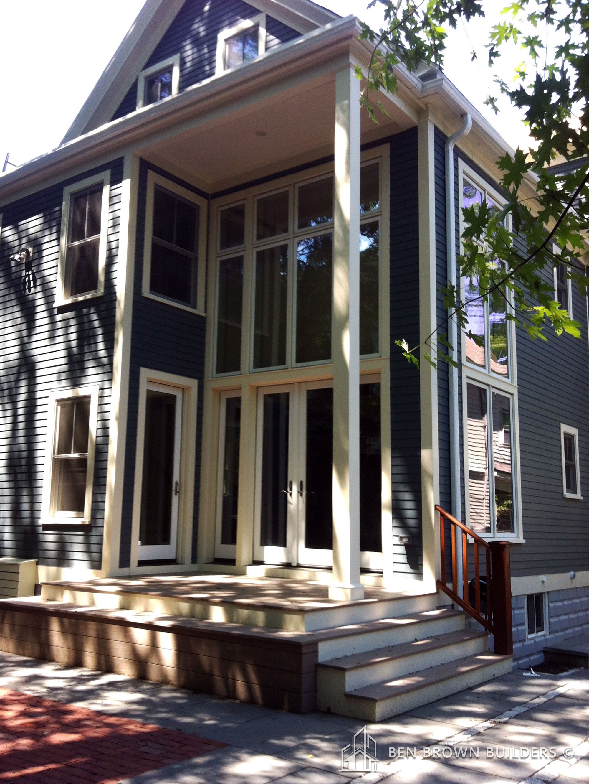 Two-story house with gray siding, white trim, large windows, and a small front porch with steps and a handrail