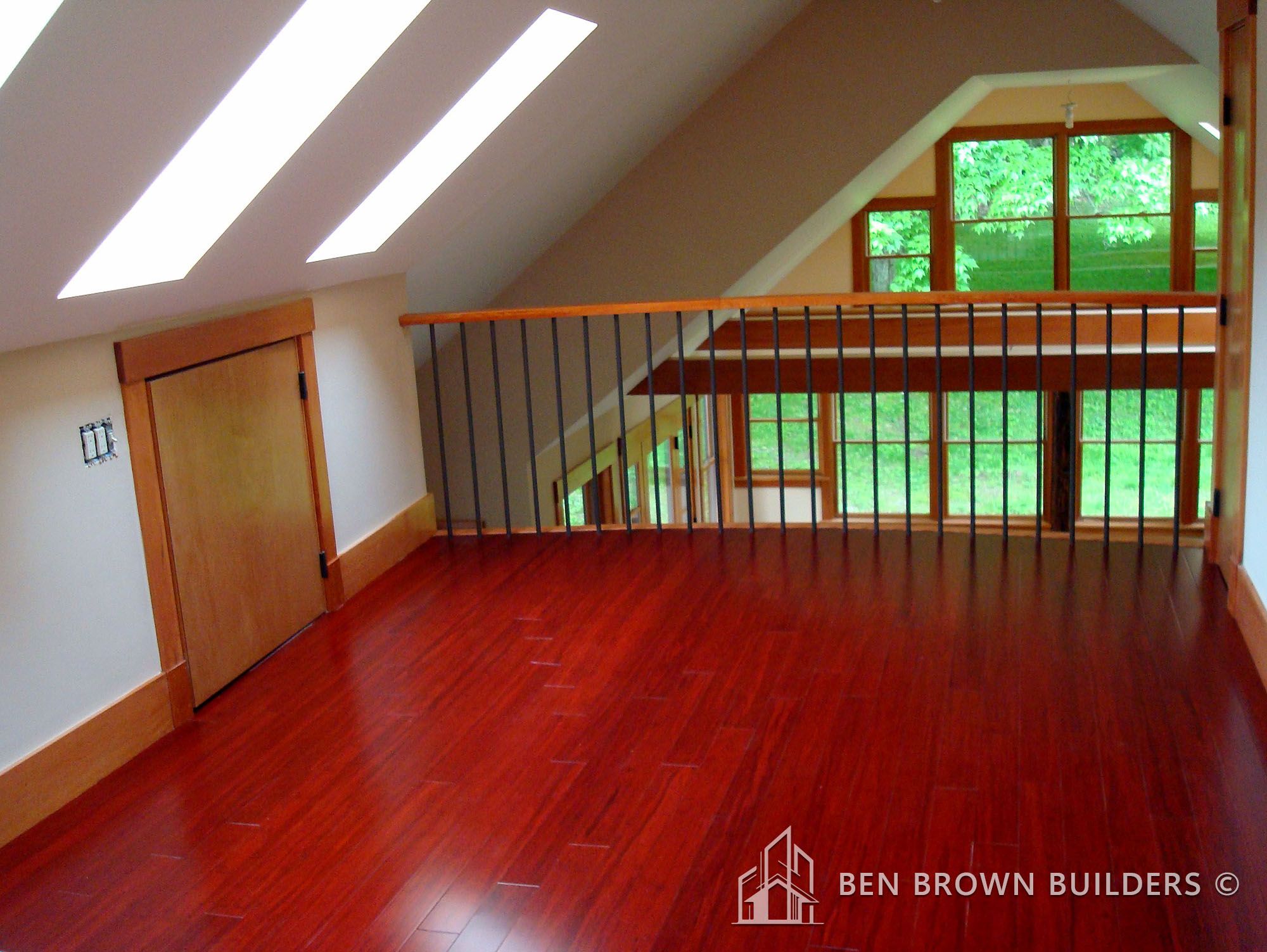 Spacious upper level room with cherry wood flooring, skylights, metal balusters, and a view of greenery outside