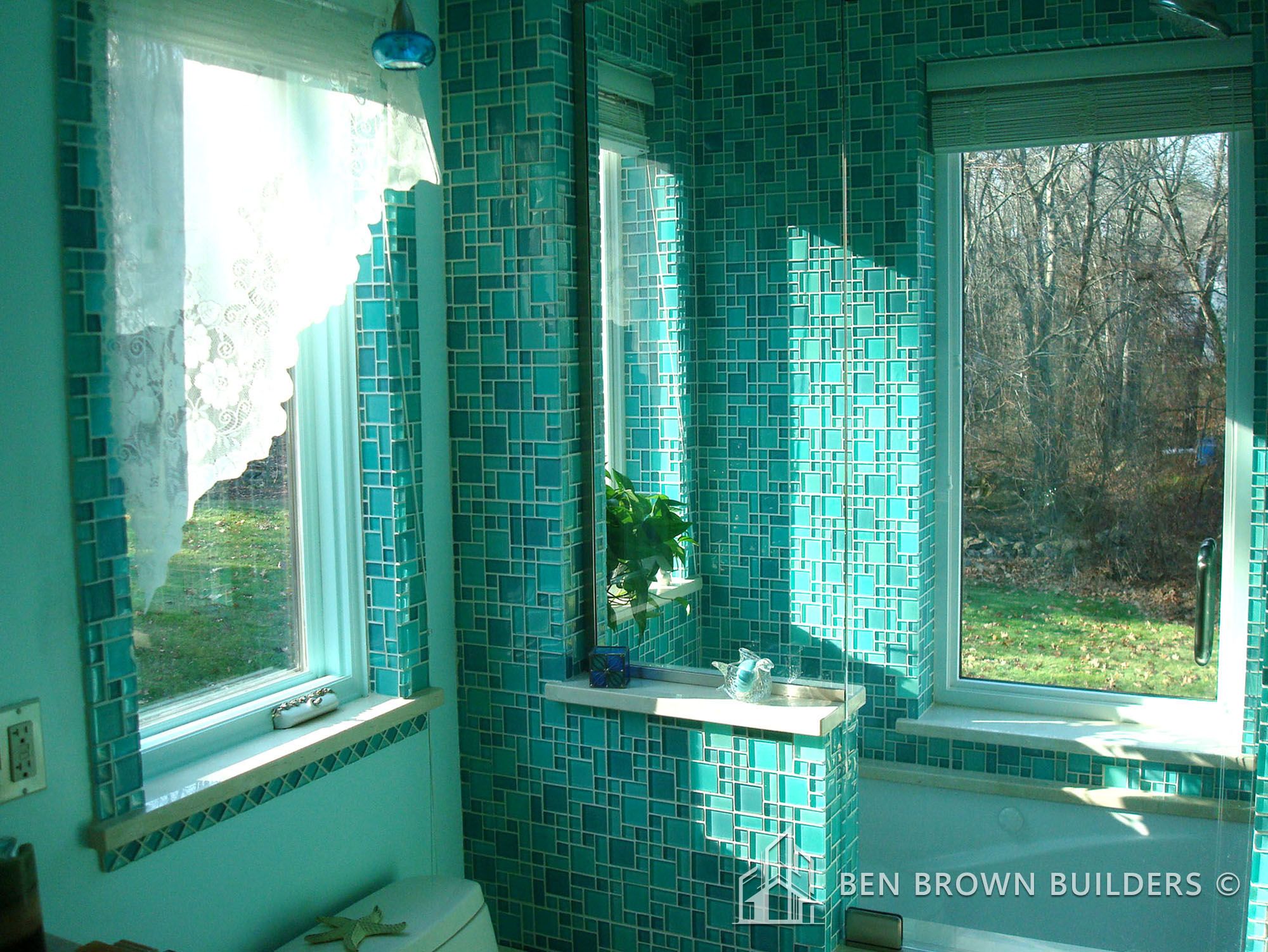 Bright bathroom with turquoise mosaic tiles, a white bathtub, lace curtains, and a view of the outdoors