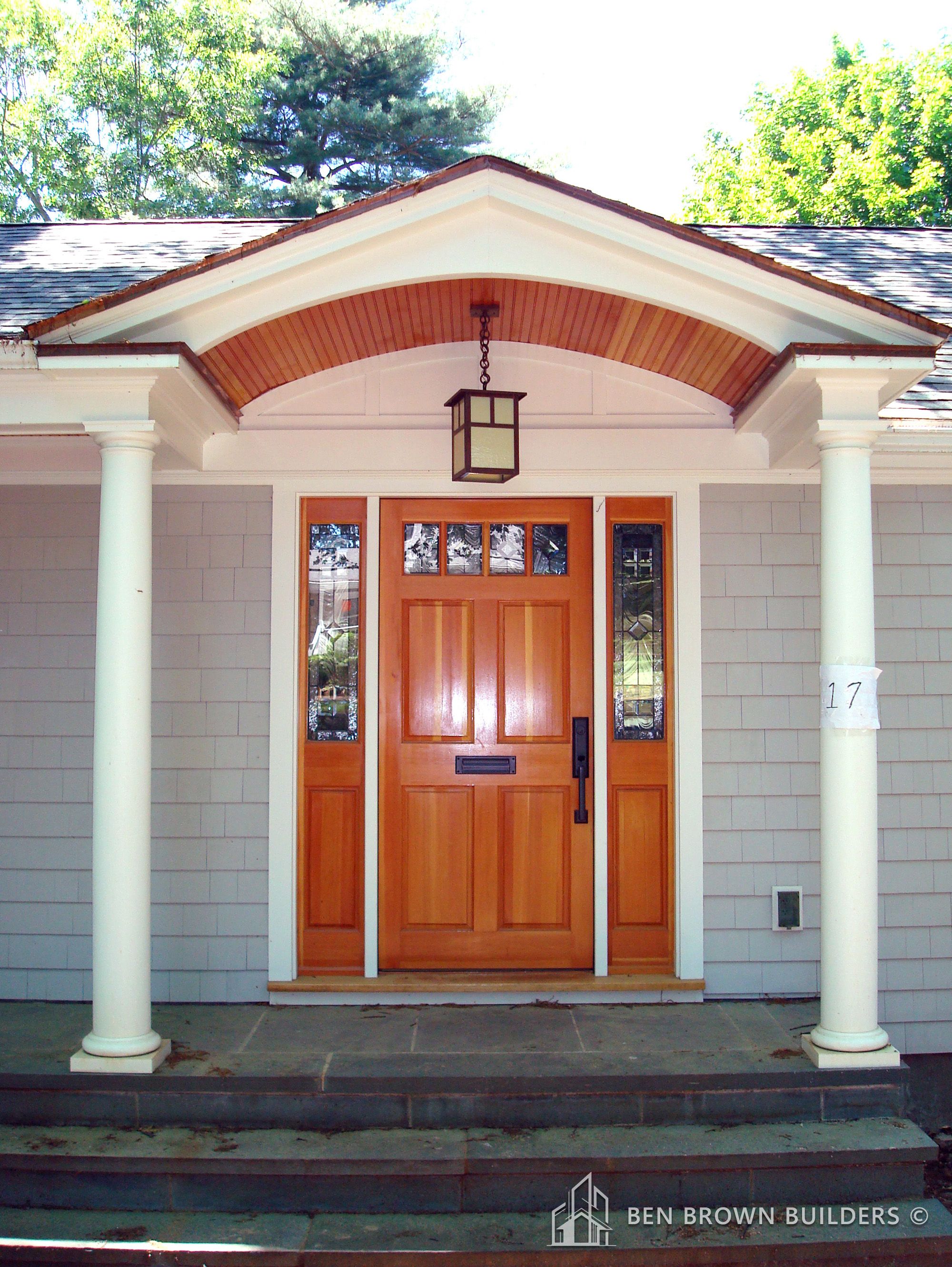 Elegant home entrance featuring a wooden door with sidelights, flanked by white columns and a hanging lantern.