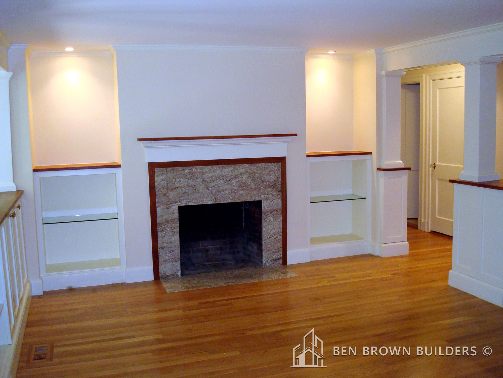 Spacious room with polished hardwood floors, white wainscoting, built-in shelves, and a granite fireplace.
