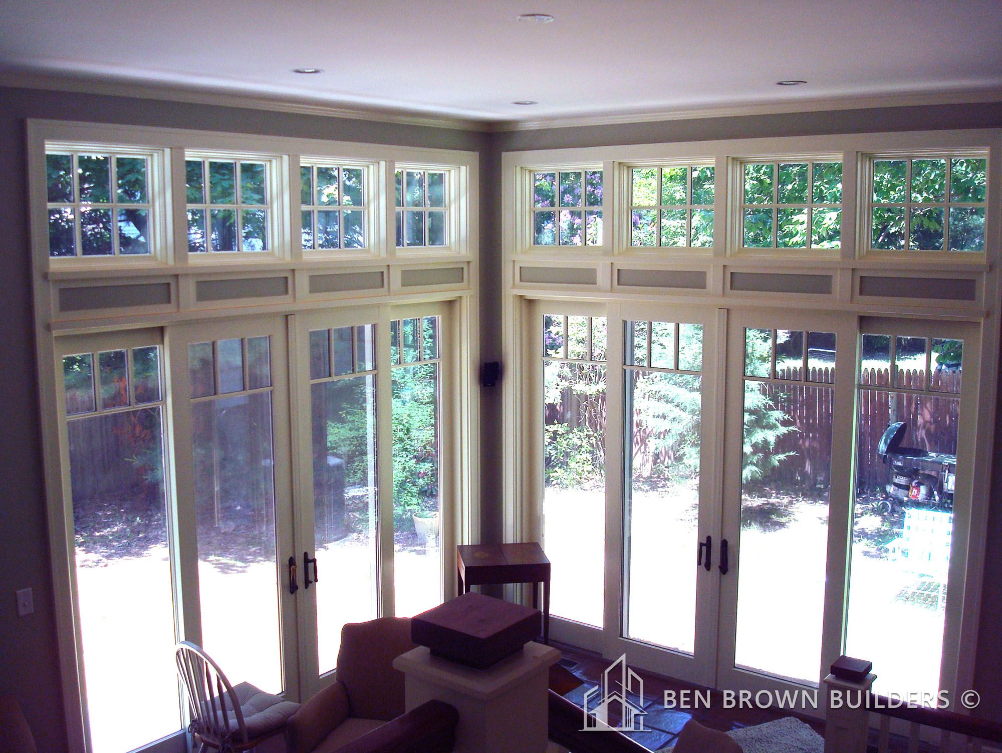 Bright sunroom with transom windows above glass doors leading to a garden with a privacy fence.