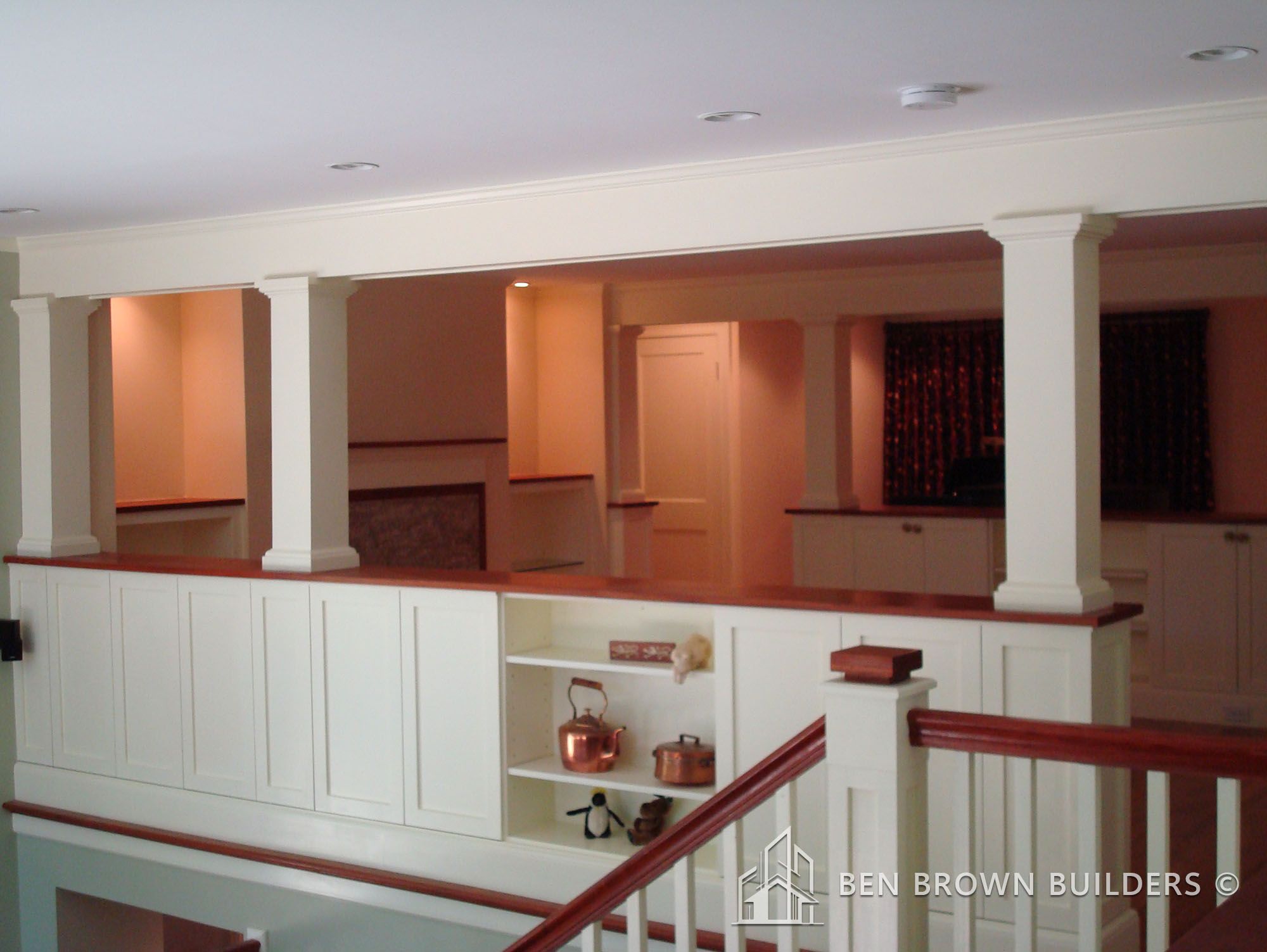 Elegant home interior with white columns, balustrades, and built-in cabinetry under warm ambient lighting.