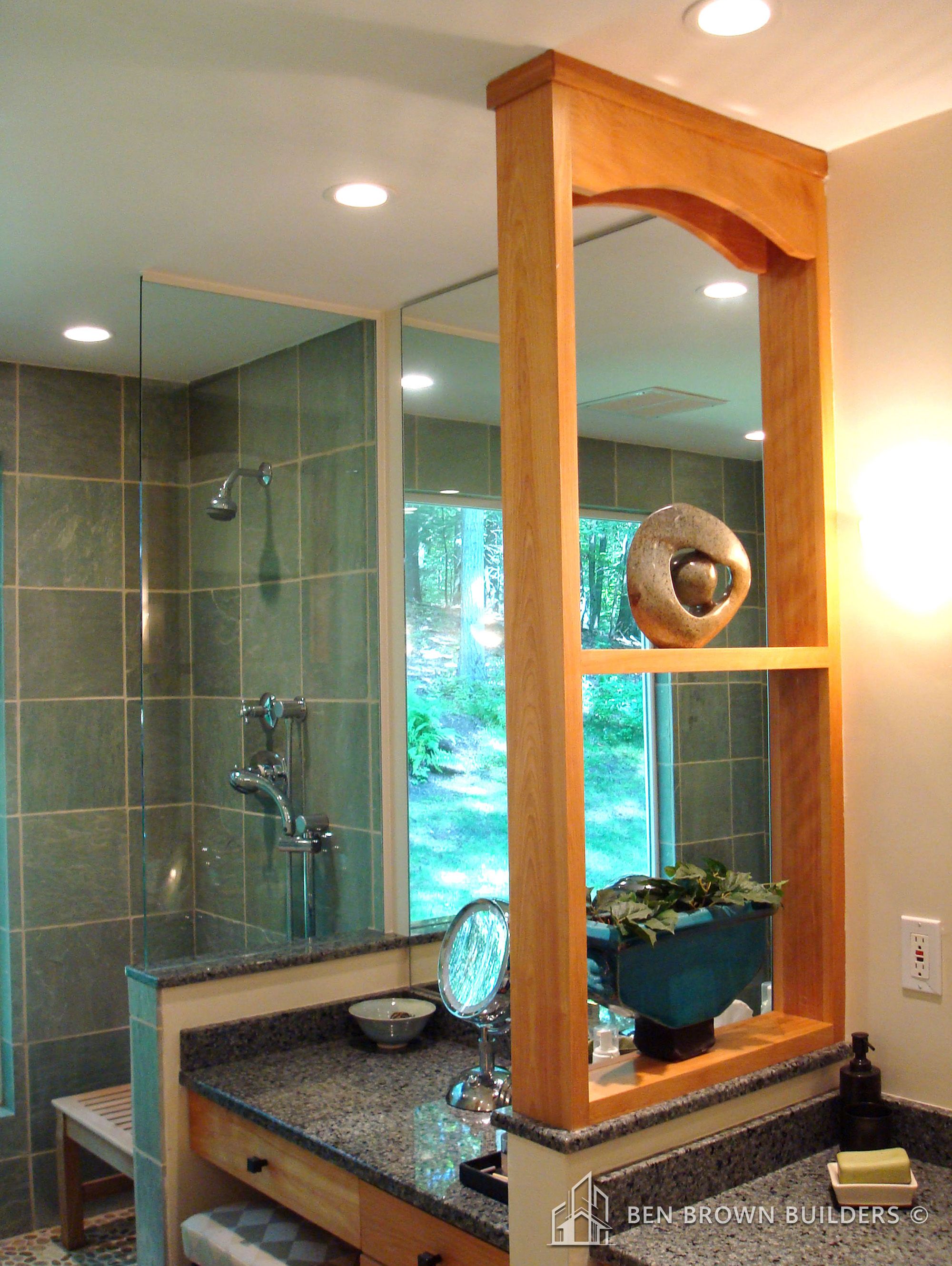 Natural light filled bathroom with green tiles, wooden mirror frame, granite countertop, and a view of trees