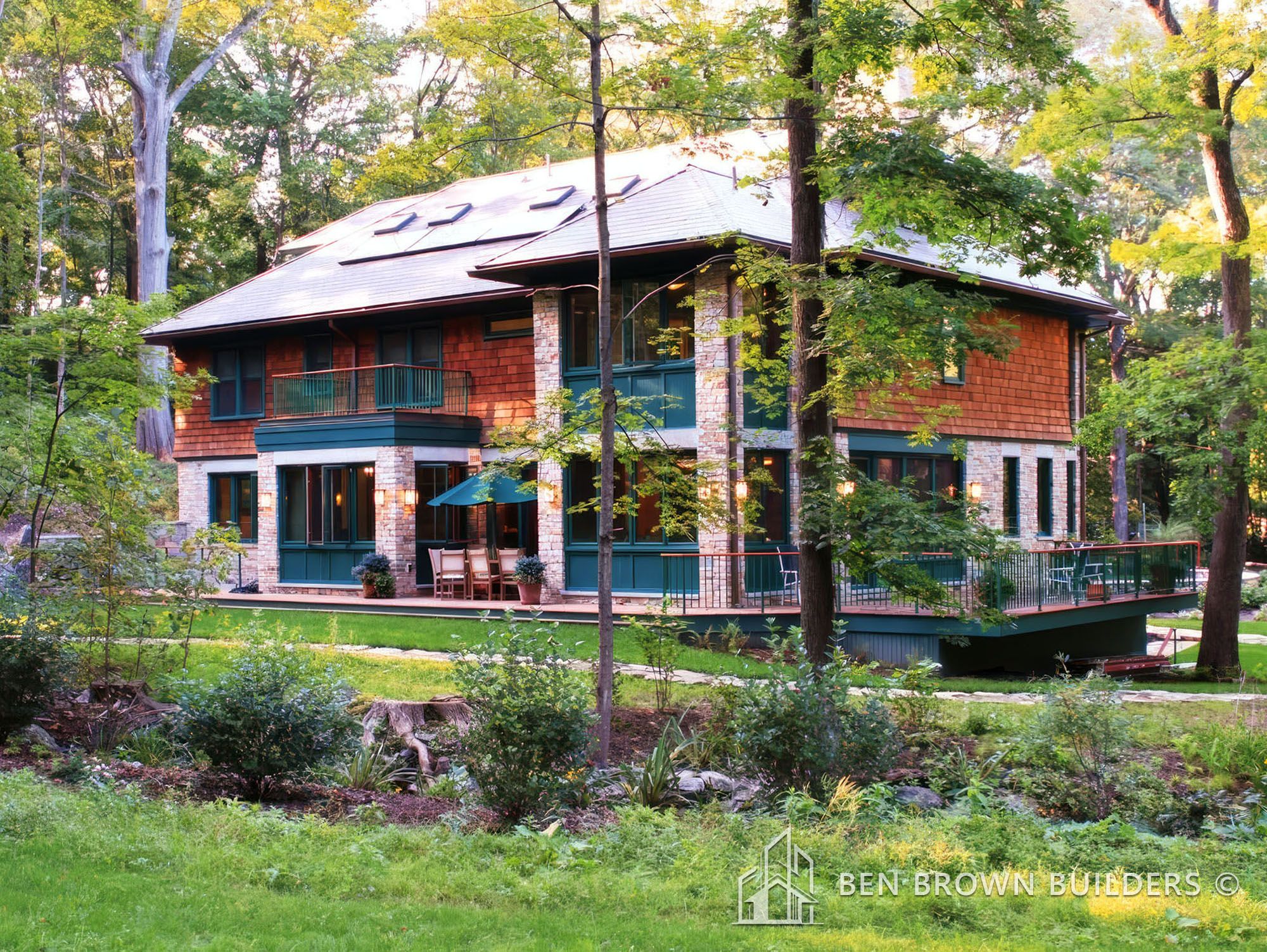 Luxurious two-story house with brick and stone facade, surrounded by lush greenery and mature trees