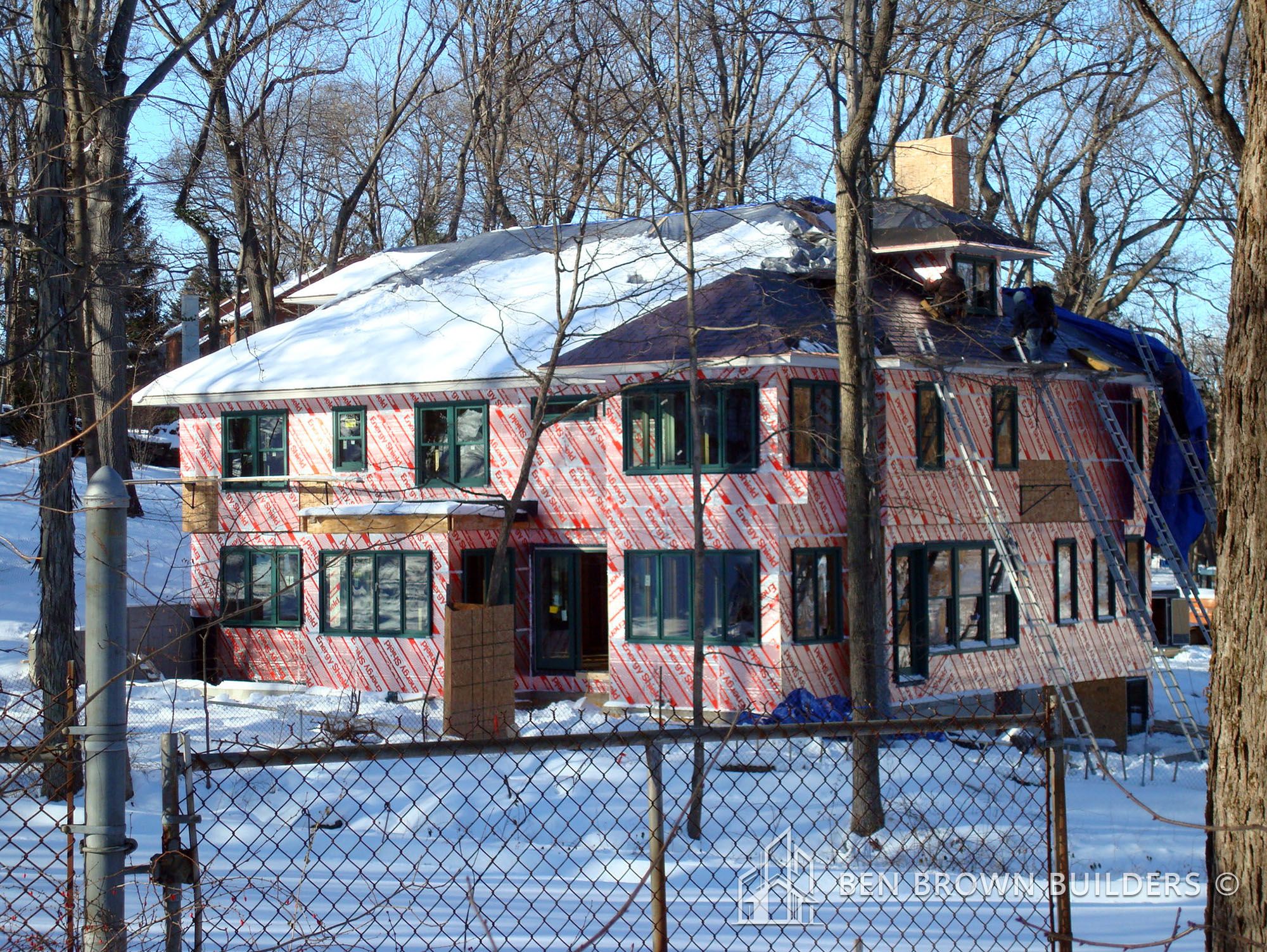 Construction of a multi-story house in winter with snow-covered roof and Tyvek house wrap on the exterior.