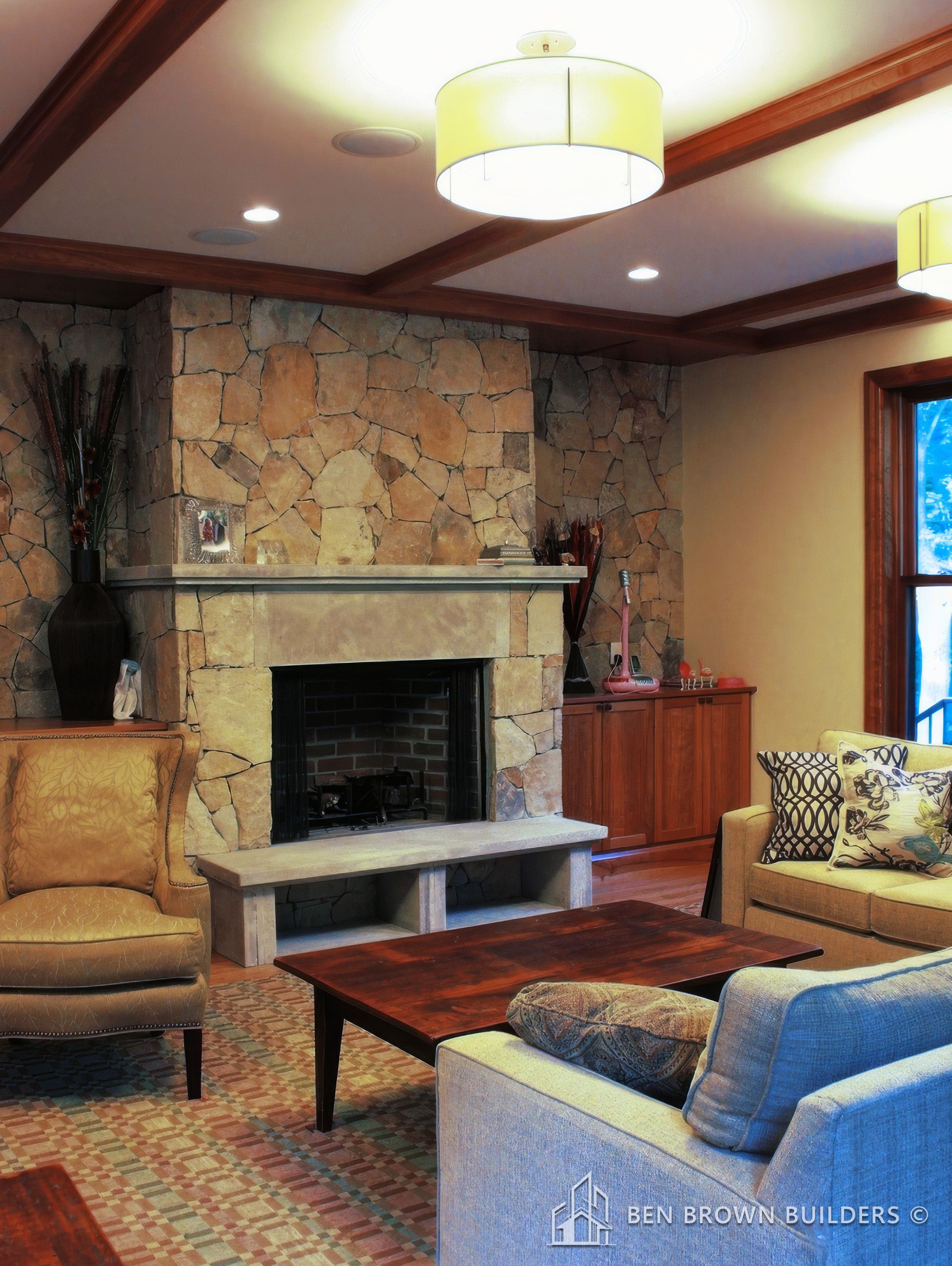 Cozy living room with a stone fireplace, wooden ceiling beams, plush furniture, and elegant lighting.