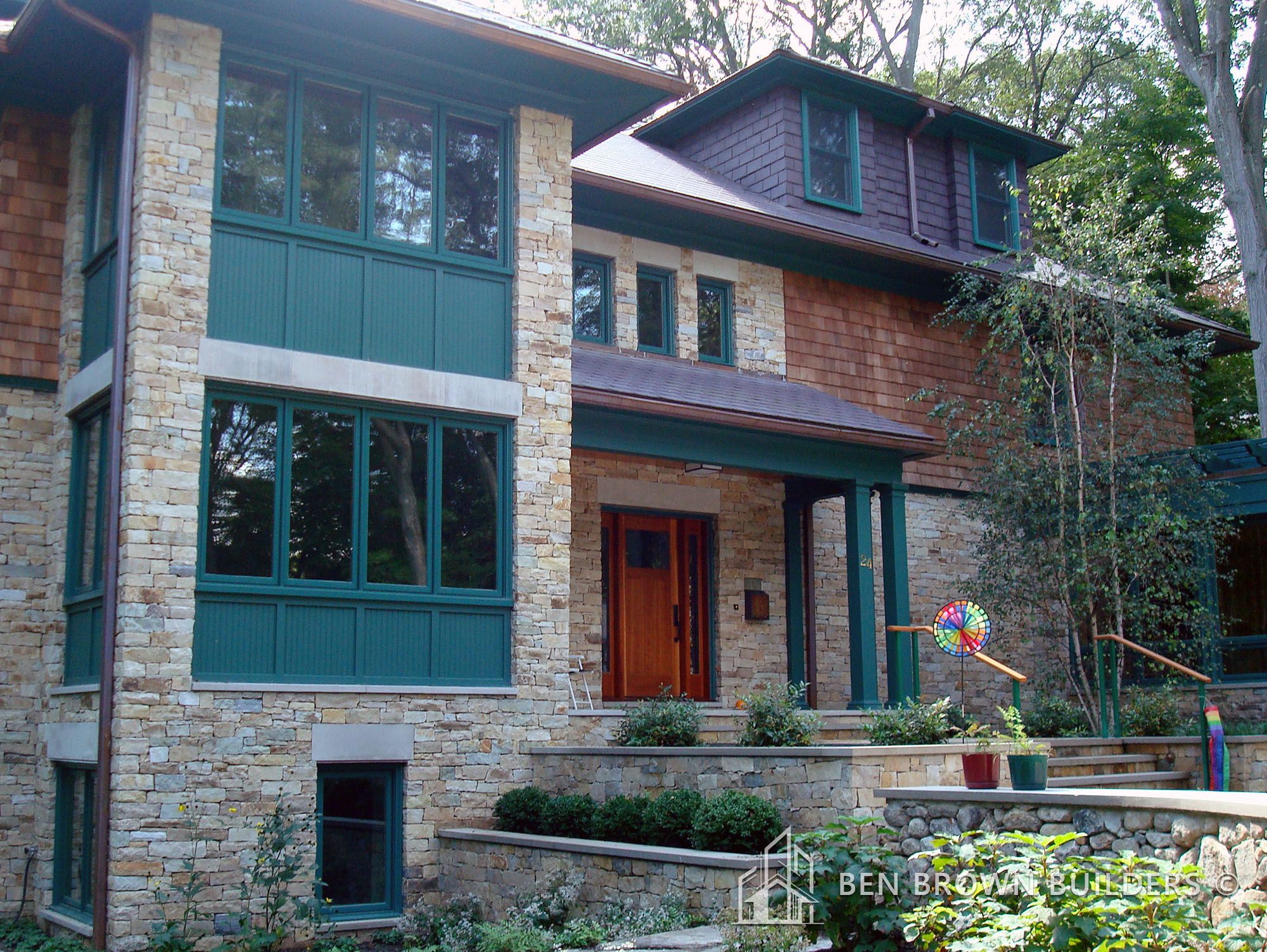 Craftsman style home with stone and wood exterior, large green window shutters, and lush surrounding foliage.