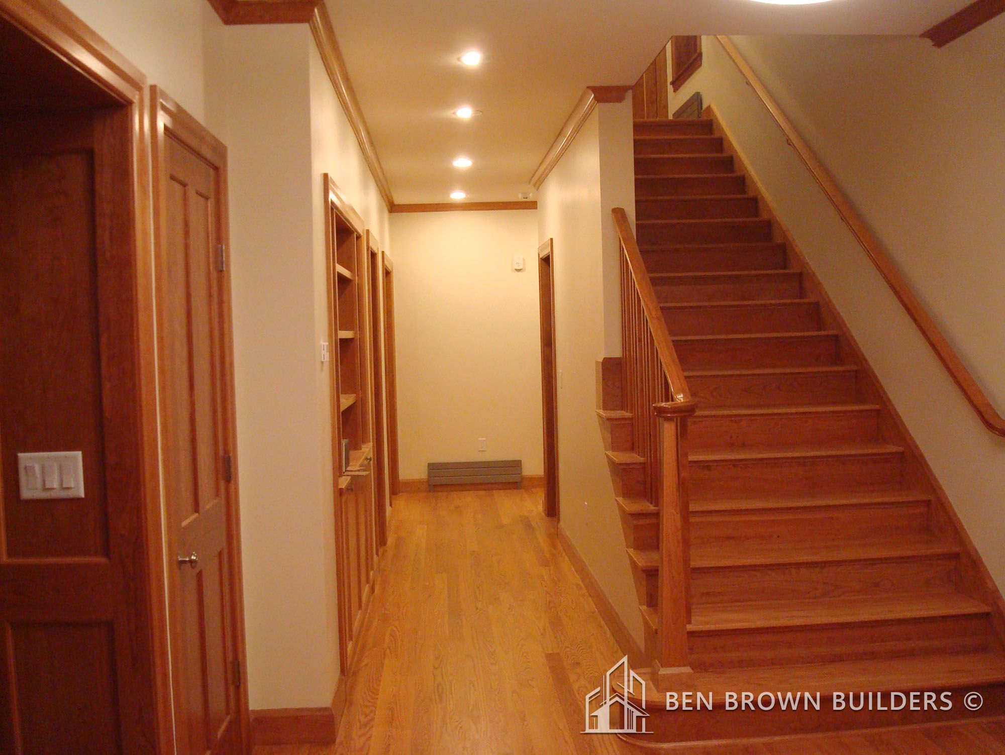 Hallway with hardwood flooring, wooden staircase, and built-in bookshelves in a cozy home interior