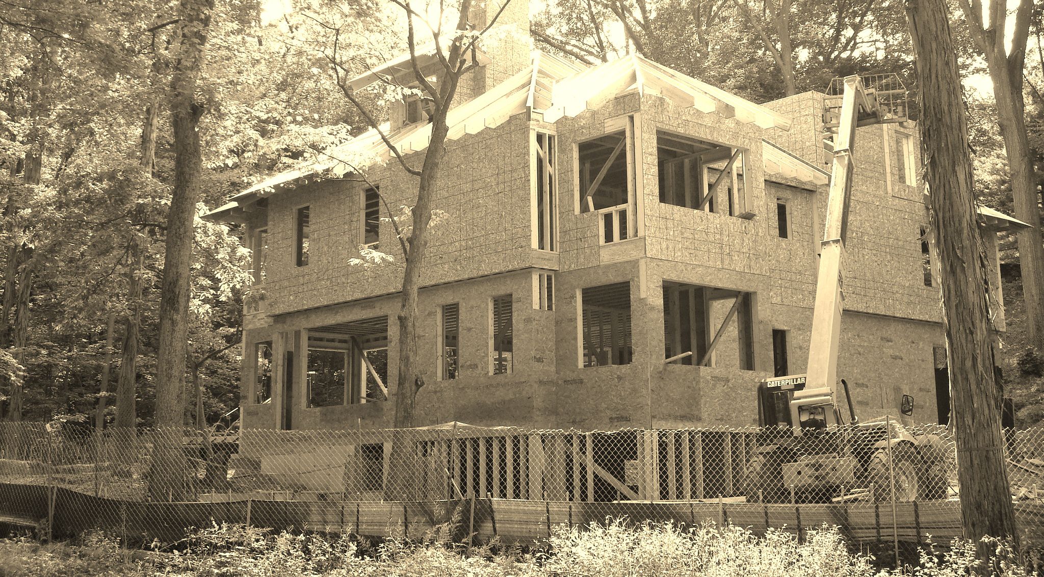 Sepia-toned image of a house under construction surrounded by trees with scaffolding and a ladder