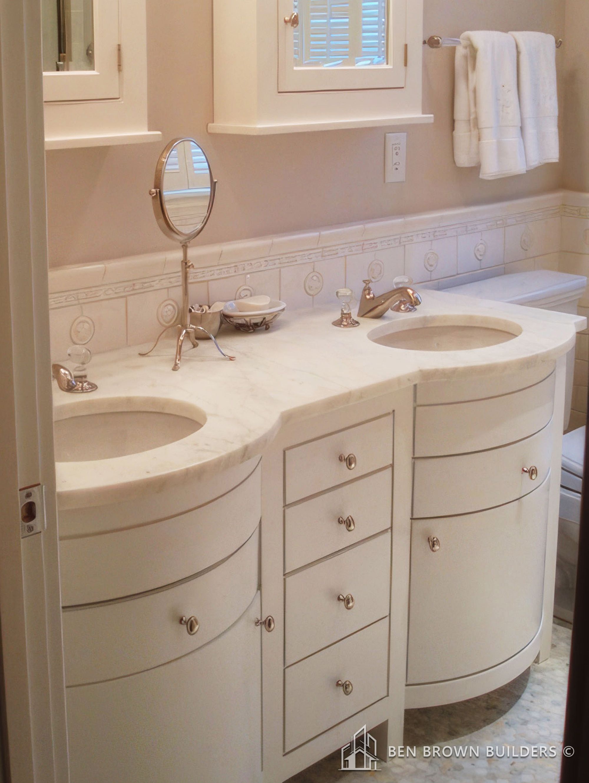 Elegant bathroom vanity area with dual sinks, white cabinetry, marble countertops, and decorative tiled backsplash