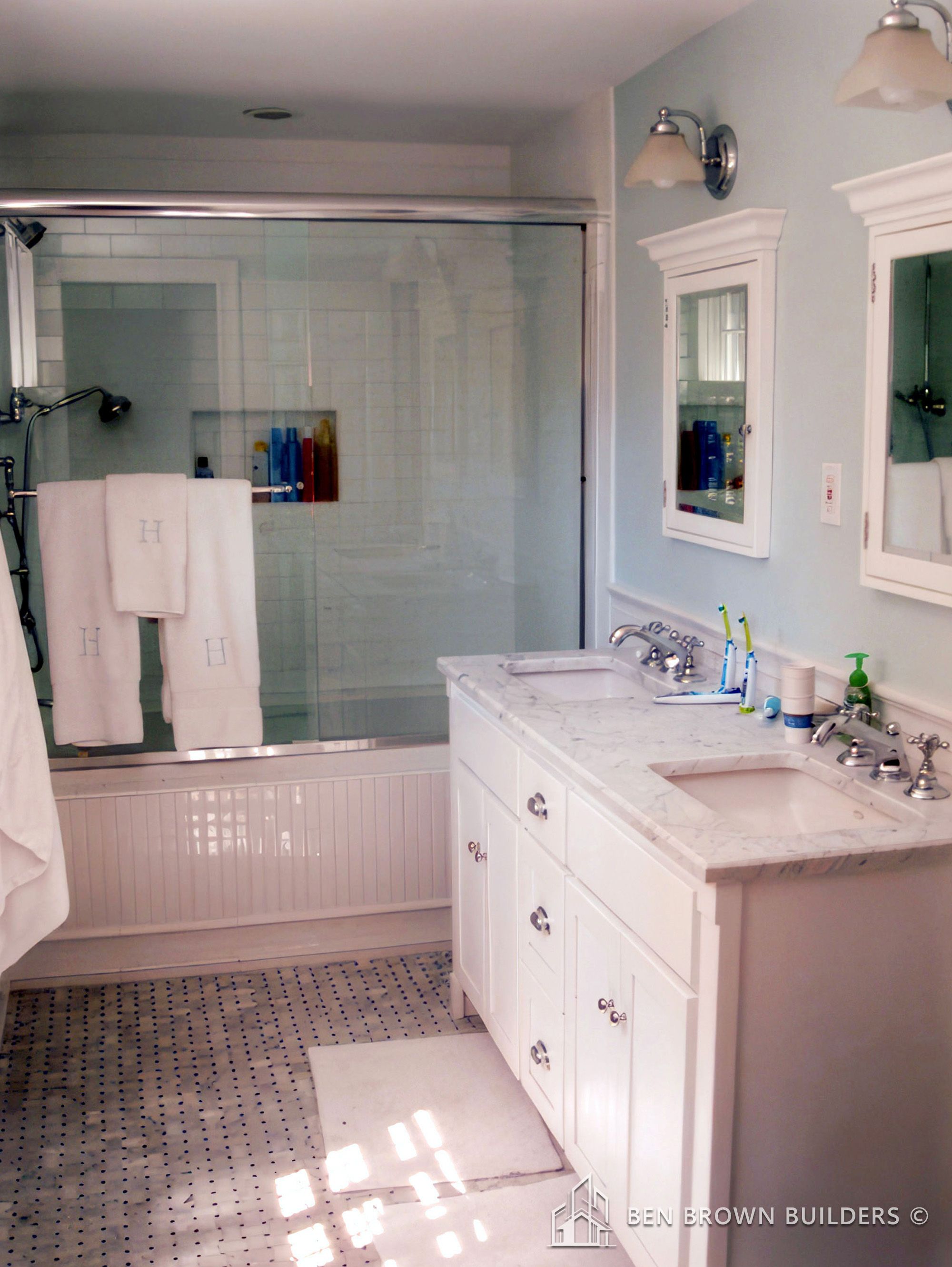 Traditional bathroom with a glass-enclosed shower, white vanity with marble top, and classic black and white floor tiles