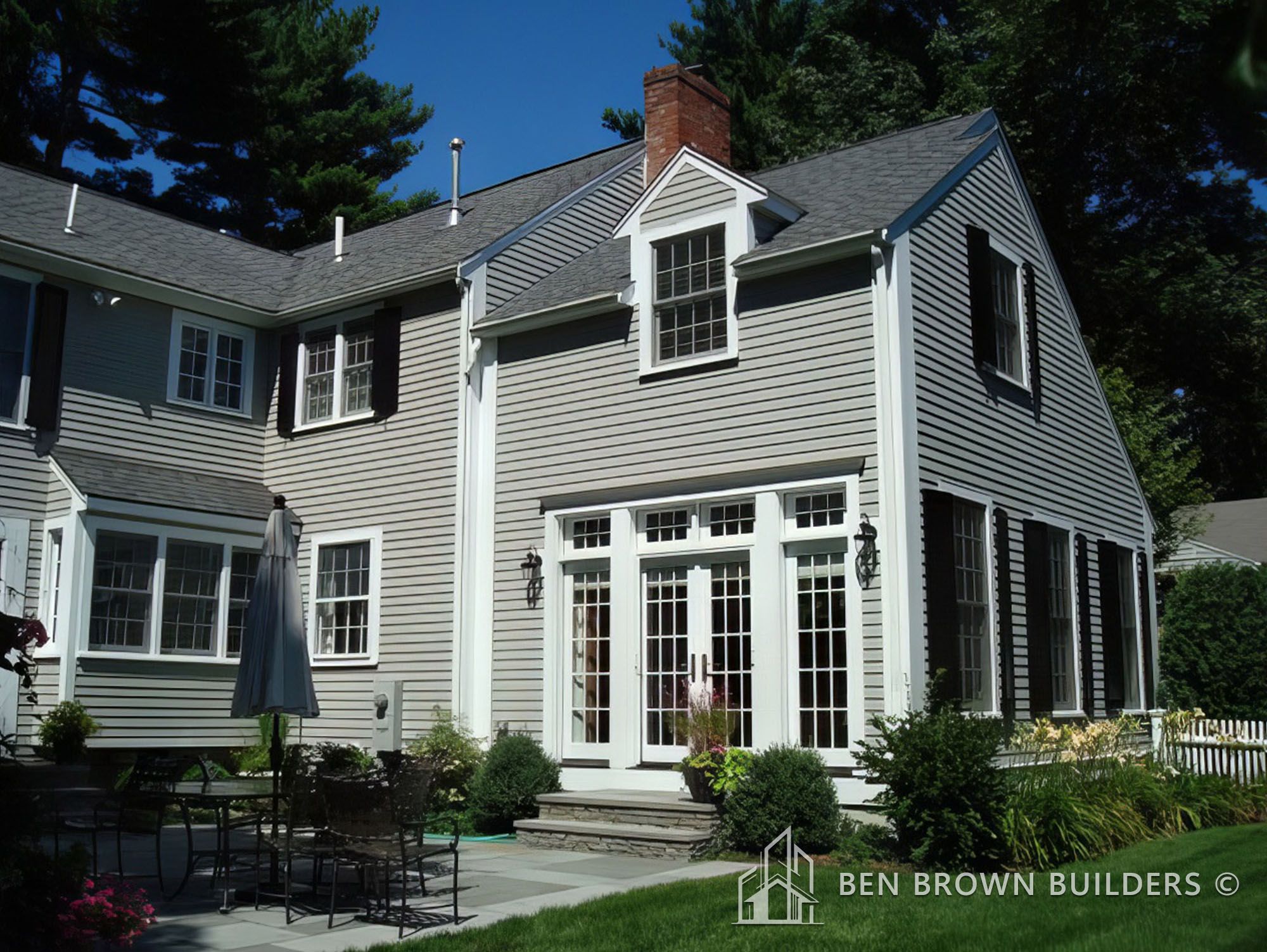 Traditional colonial-style home with beige siding, white trim, and a well-manicured lawn with patio area