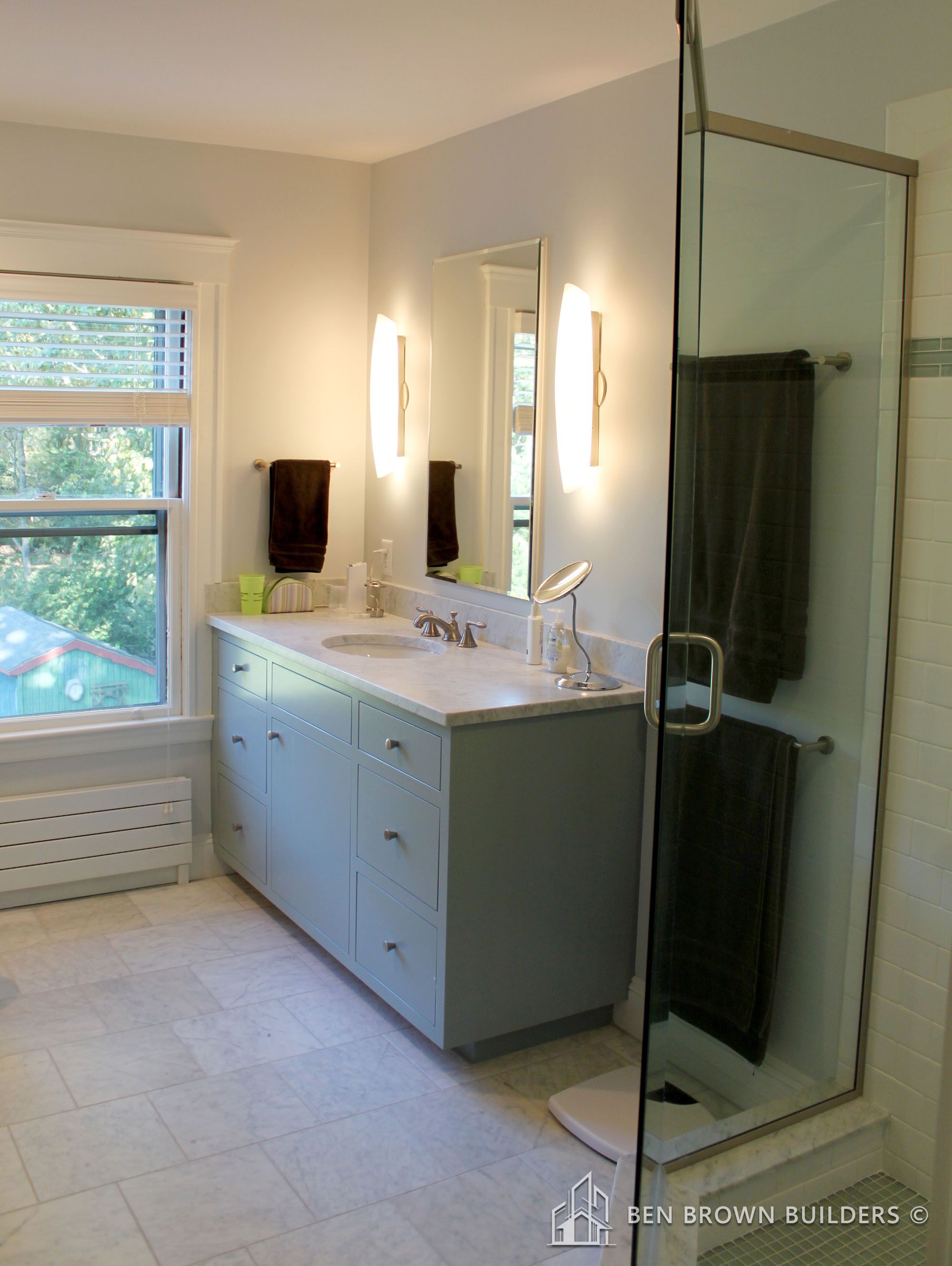 Bright bathroom interior with a marble-top vanity, dual sconces, and a glass-enclosed shower area.