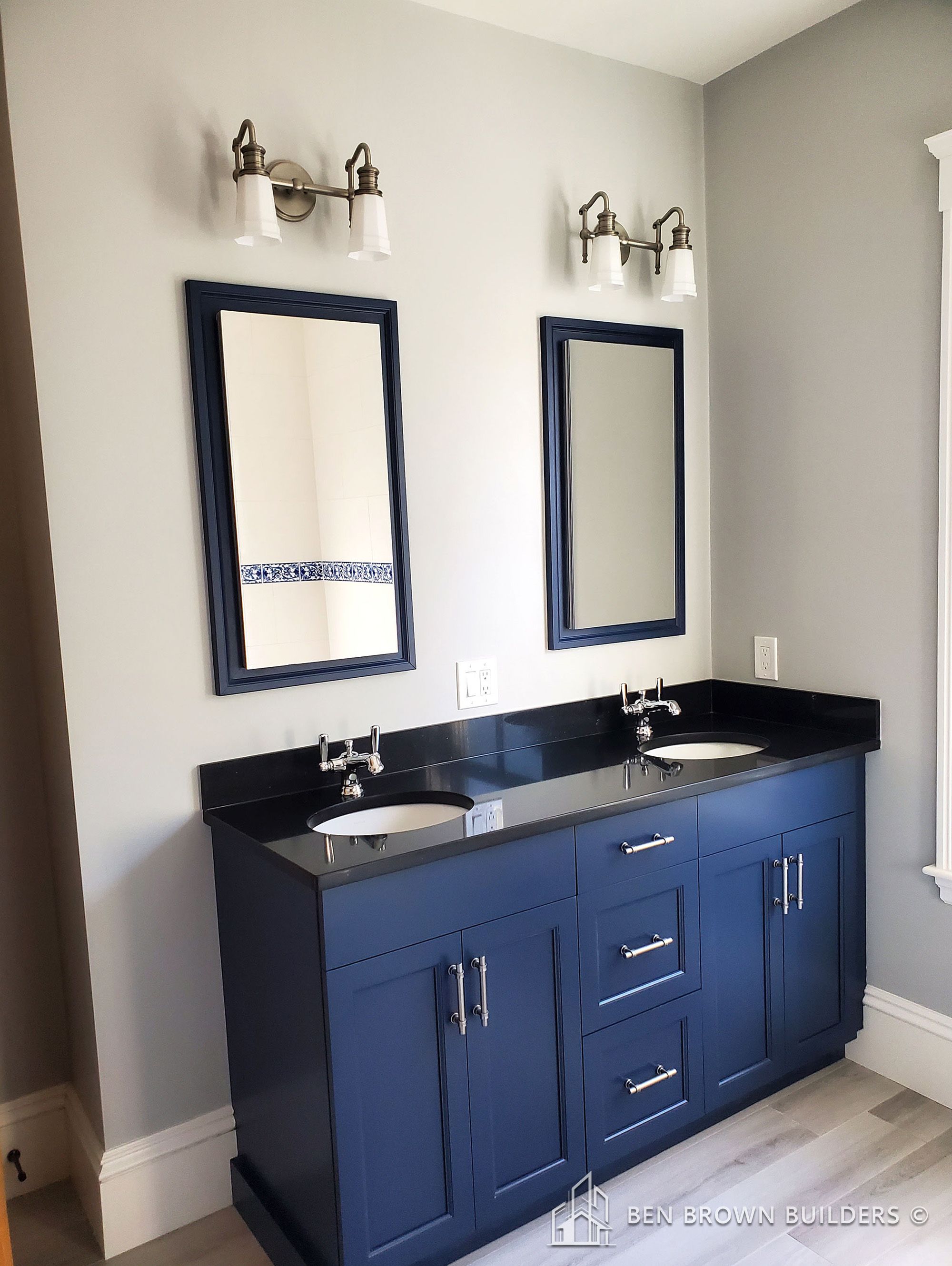Chic bathroom with a navy blue vanity, double sinks, two framed mirrors, and vintage-style wall sconces