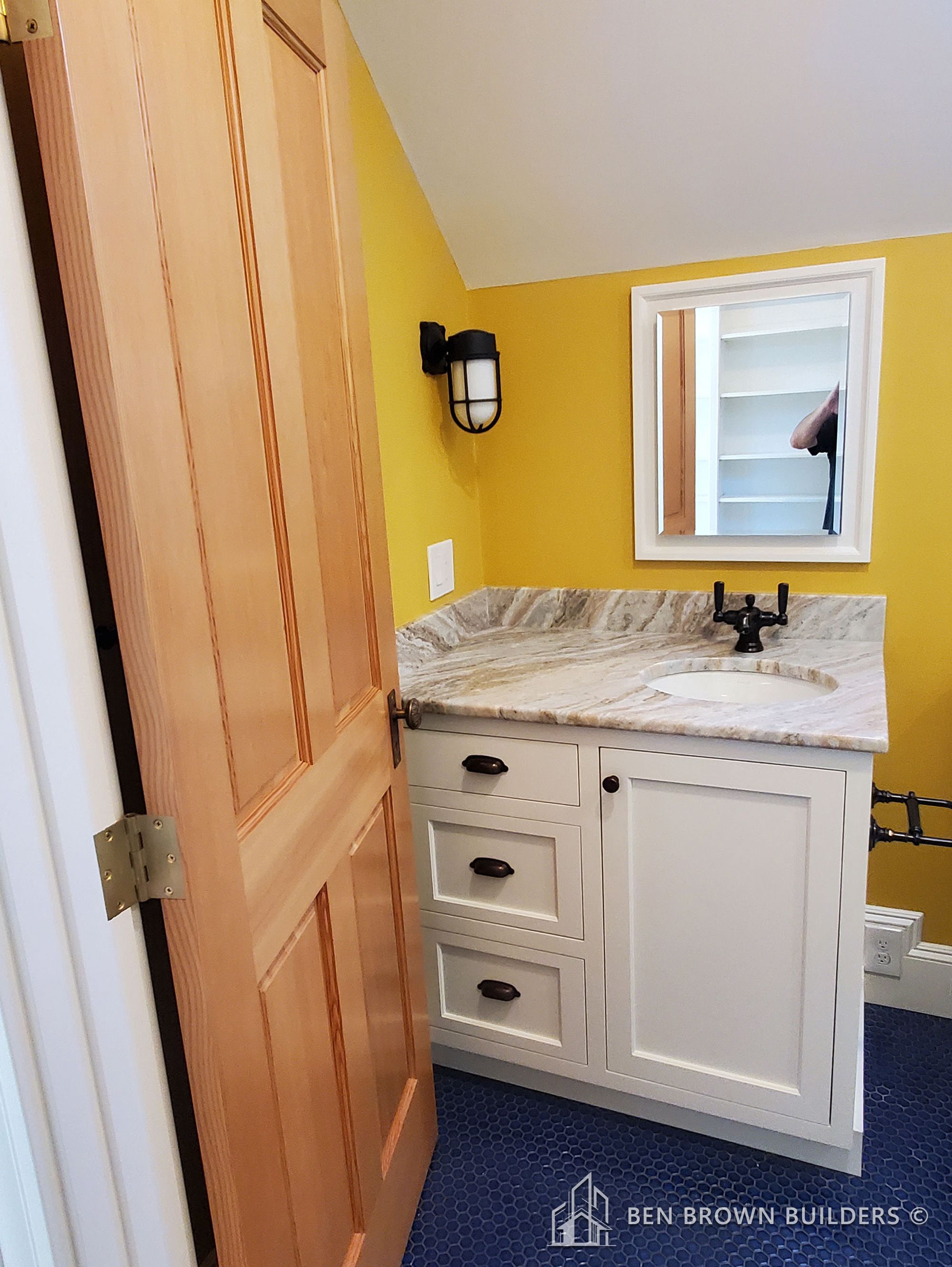 Bright bathroom corner with a vivid yellow wall, white vanity cabinet, marble countertop, and hexagonal floor tiles