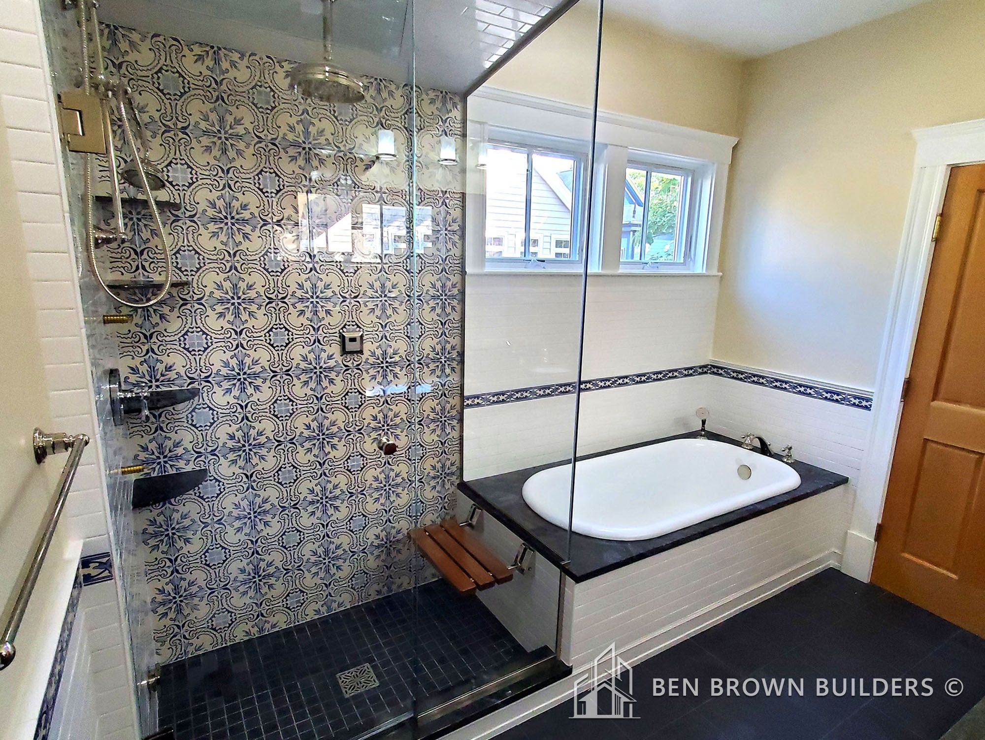 Modern bathroom with decorative blue and white tiled walls, glass shower, and built-in bathtub