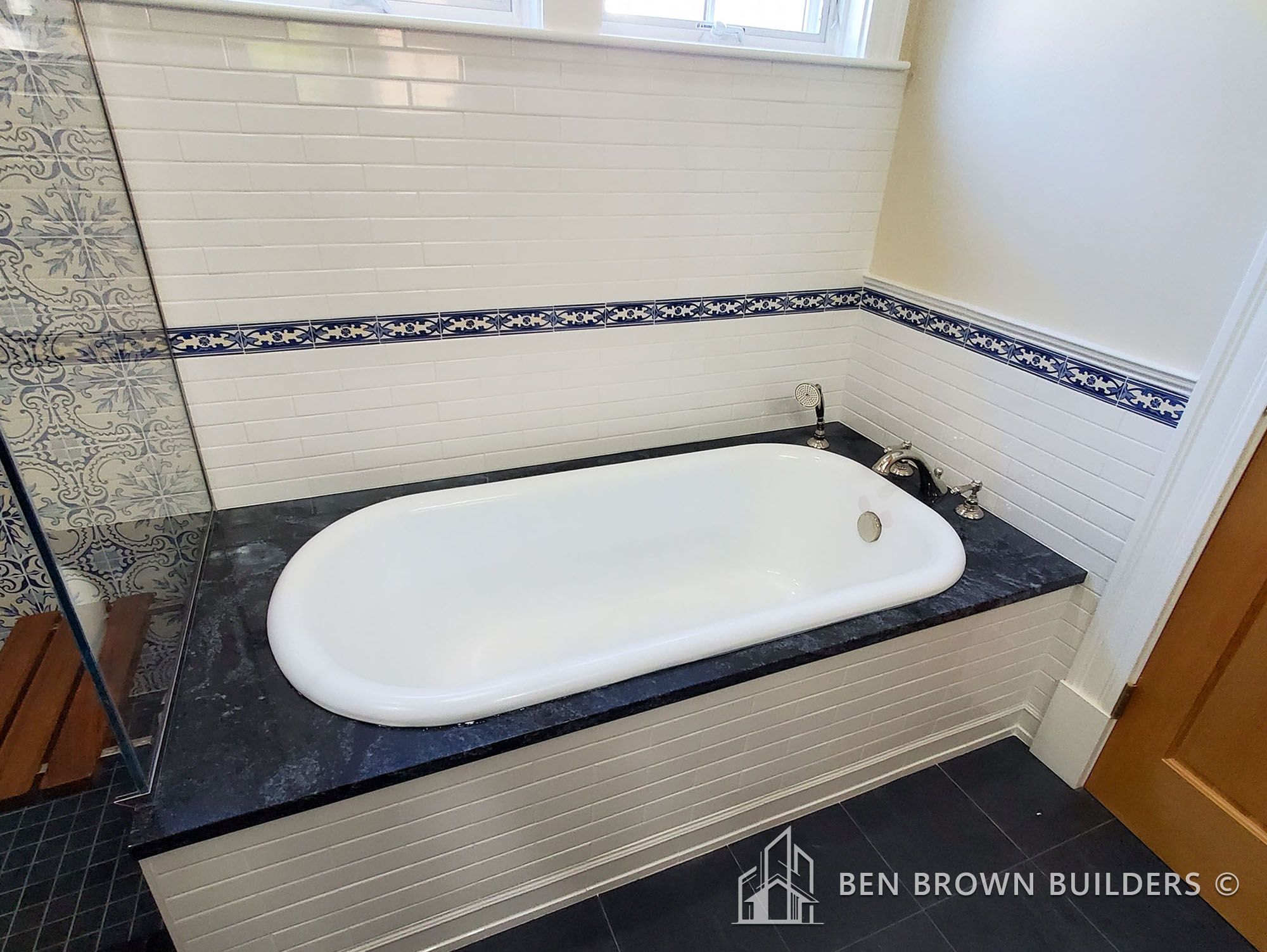 Modern bathroom with a white freestanding bathtub, ornate blue and white tiles, and dark stone floor