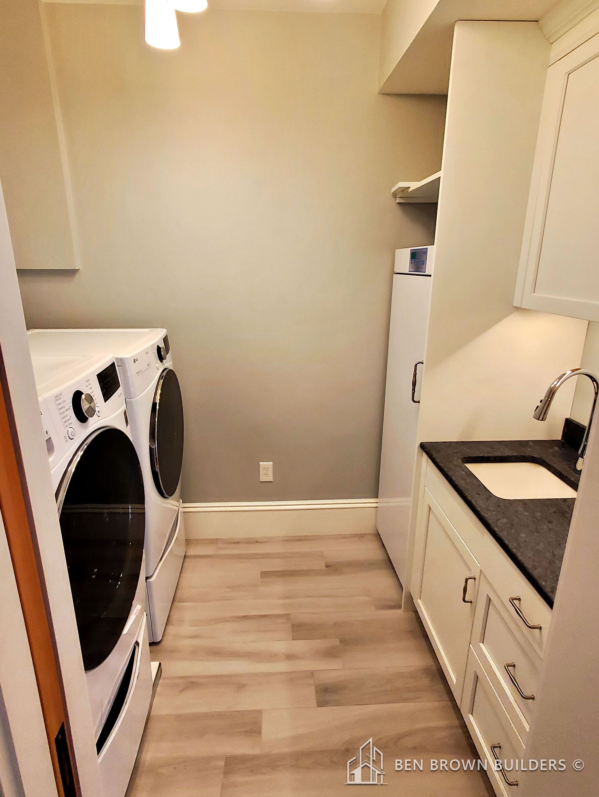 Compact laundry room with modern appliances, white cabinets, grey countertop, and light wooden flooring