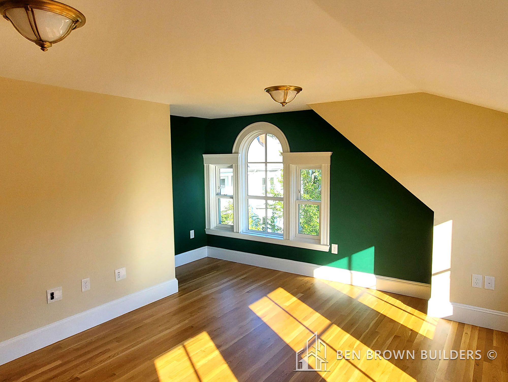 Bright room with a slanted ceiling, hardwood floors, and a deep green accent wall with arched window