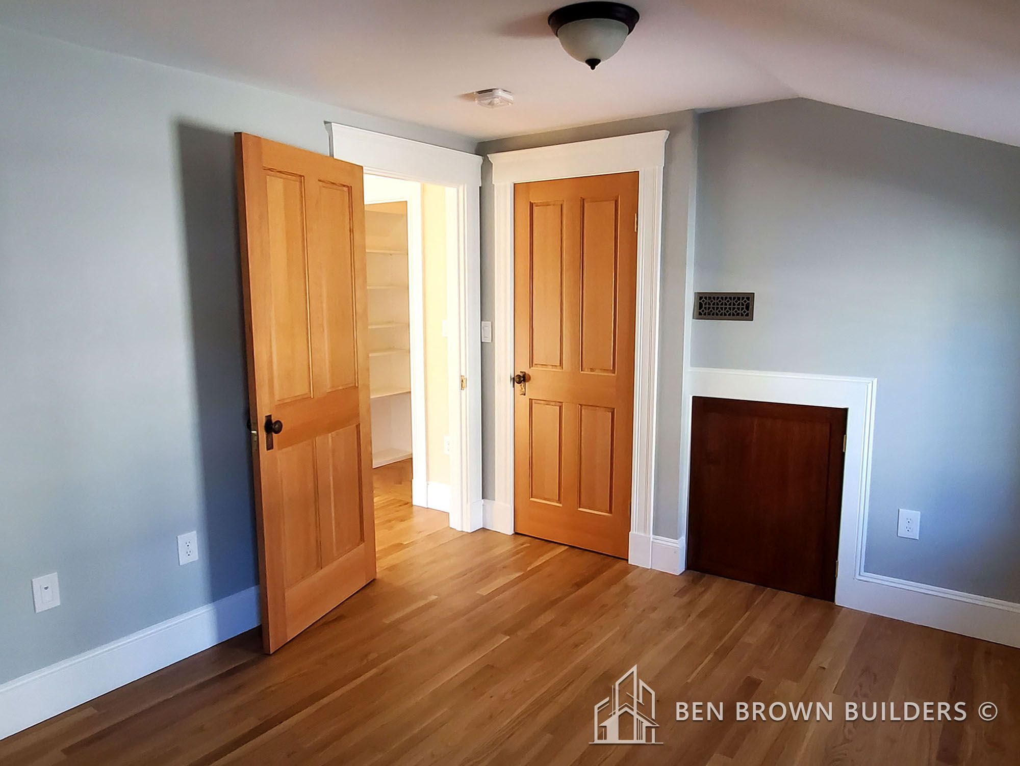 Corner of a room with light blue walls, hardwood floor, wooden doors, and a small built-in cabinet