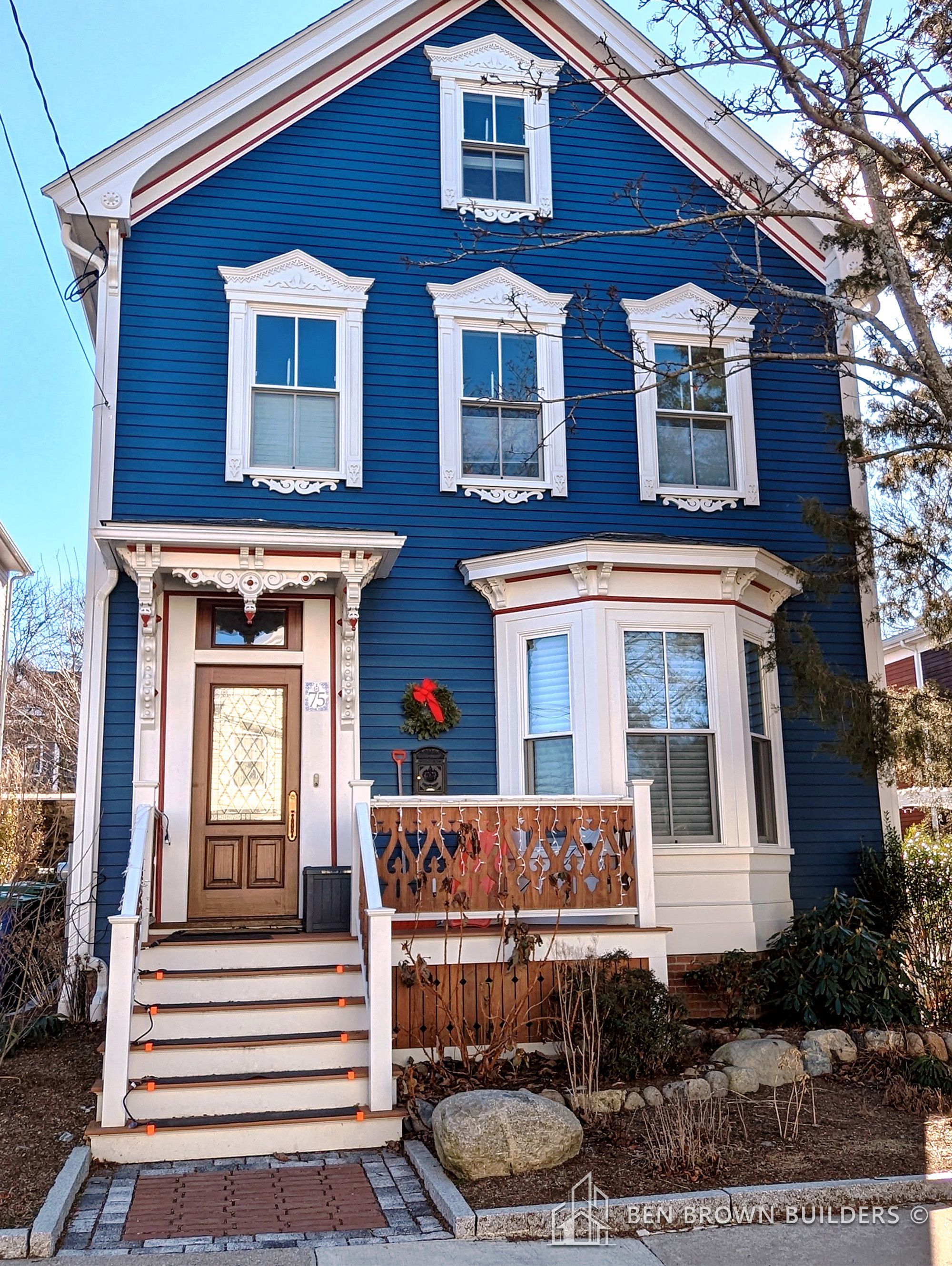 Vibrant blue multi-story home with white trim and a quaint red shed, under a clear blue sky