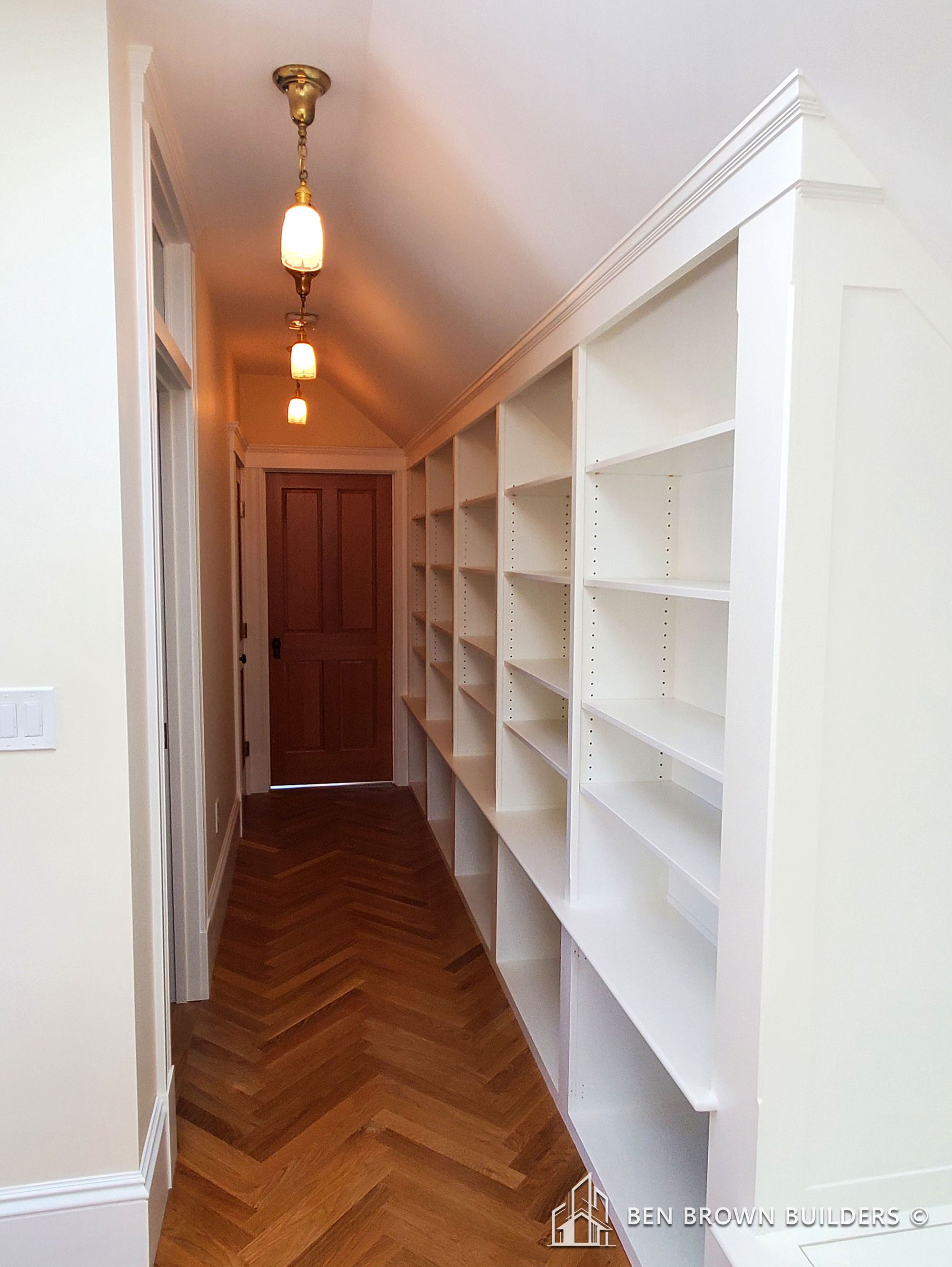 Narrow hallway with herringbone wood flooring, built-in white bookshelves, and vintage hanging lights