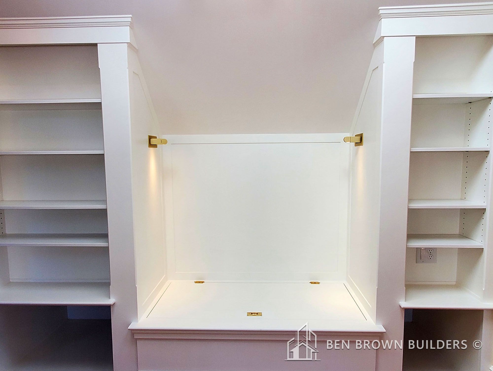 Built-in white nook with a bench and storage shelves, accented with brass hardware, in a modern home