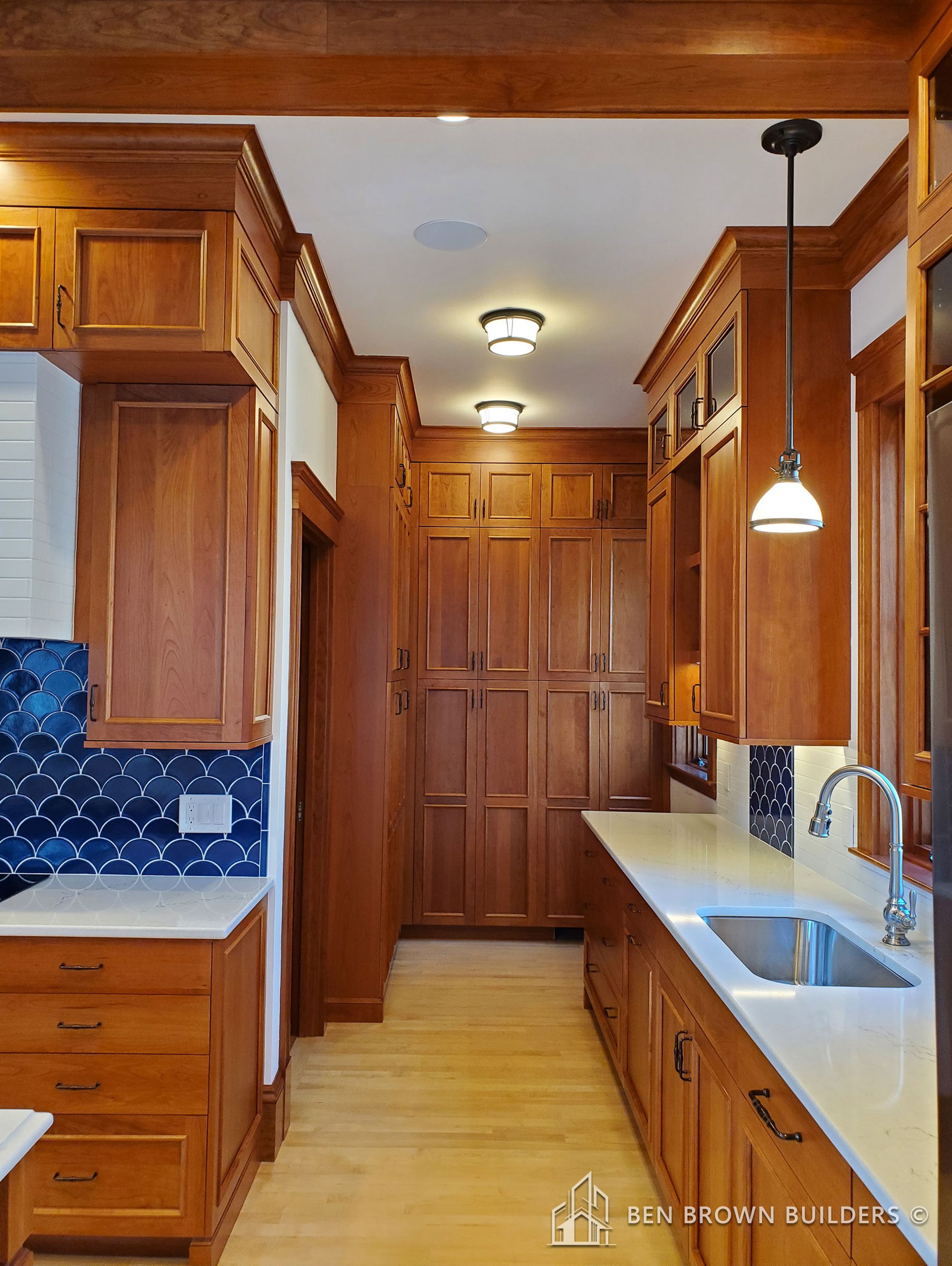 Elegant kitchen corridor with rich wooden cabinets, hardwood floors, and detailed tile backsplash