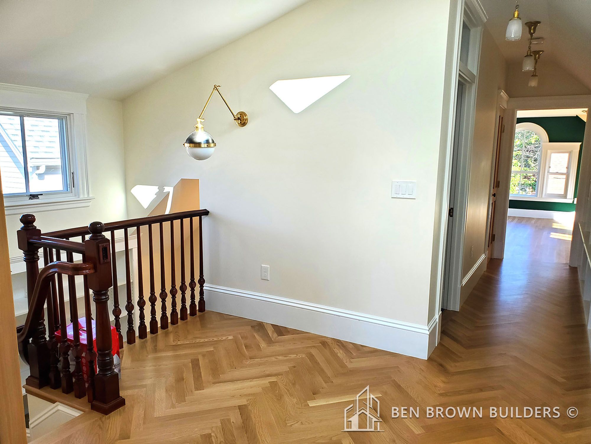 Spacious upper landing with herringbone wood flooring, elegant balustrade, and chic wall-mounted lights
