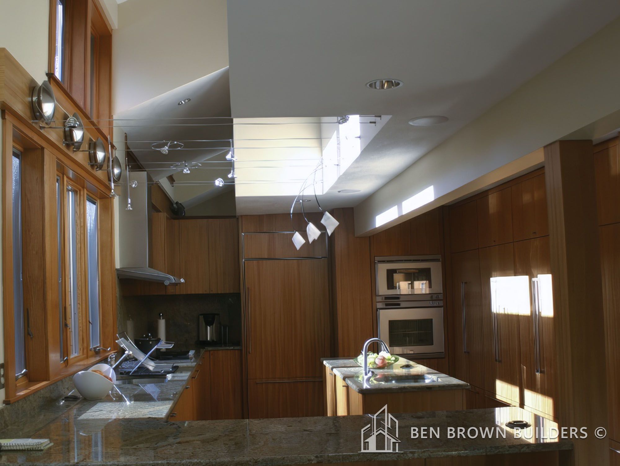 Modern kitchen with wooden cabinetry, granite countertops, and unique ceiling-mounted light fixtures