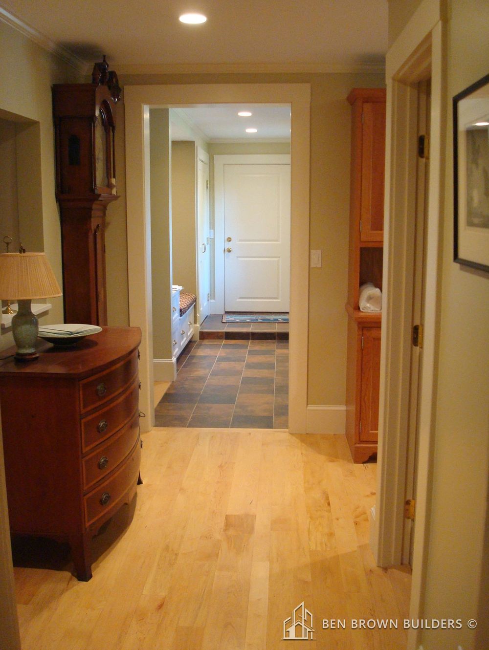 Cozy hallway with natural hardwood floors, wooden furniture, and soft lighting leading to a tiled area