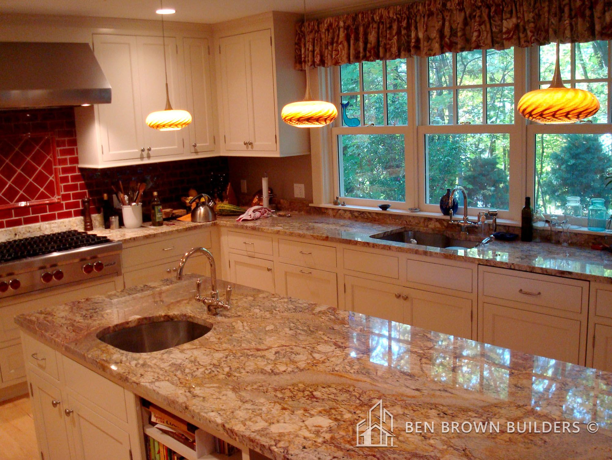 Elegant kitchen with cream cabinets, granite countertops, red backsplash, and pendant lights