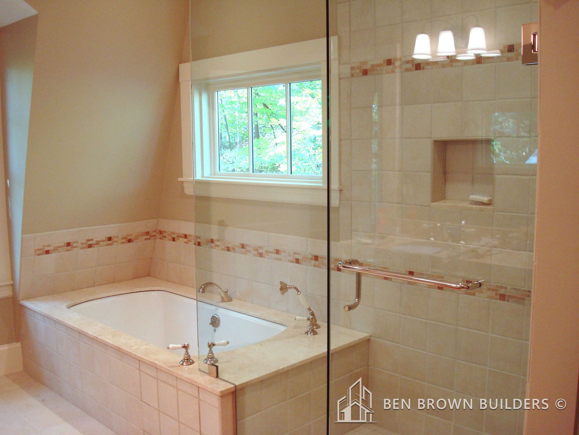 Spacious bathroom interior with a large built-in bathtub, tiled walls with decorative borders, and a glass shower area